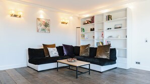 A modern living room with a sectional sofa, a coffee table, a white bookshelf, and wall-mounted lighting. - Le Belvédère - Penthouse, sea & country view (Tourgéville)