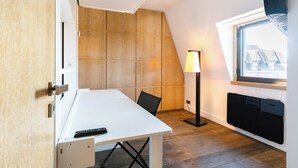 A room with a white table, a black chair, a standing lamp, and a window with a view of buildings. - Le Belvédère - Penthouse, sea & country view (Tourgéville)