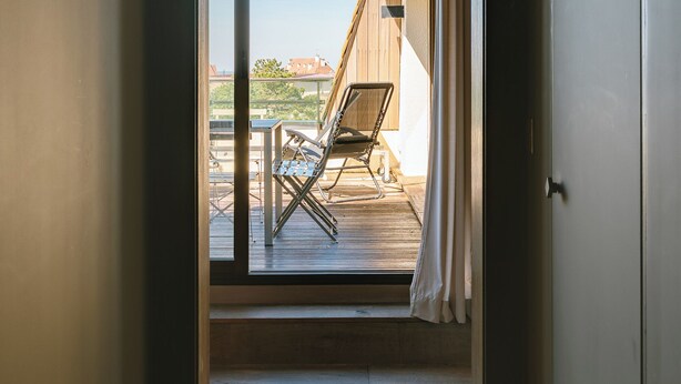 A corridor leading to a balcony with a chair and table, wooden flooring, and a view of buildings. - Le Belvédère - Penthouse, sea & country view (Tourgéville)