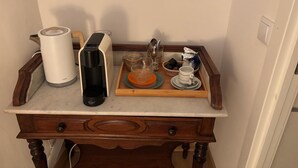 En køkkenbordplade med kaffemaskine, elkedel, bakke med kopper og teekande, samt et træbord med skuffer.