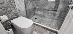 A bathroom with a marble floor, a toilet, and a shower area.