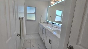 A bathroom with a white vanity, a large mirror, and a window.