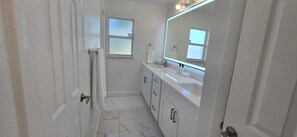 A bathroom with a white vanity, a large mirror, and a window.