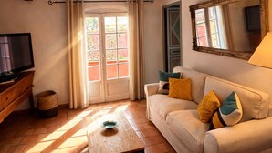 Ein Wohnzimmer mit einer Couch, einem Fernseher, einem Fenster mit Vorhängen und einem Fliesenboden.
