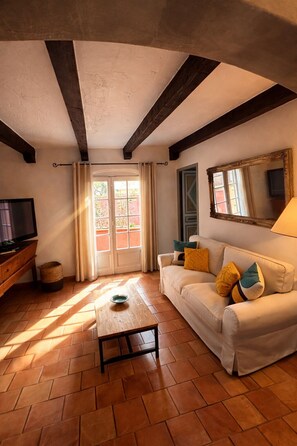 A living room with a sofa, a television, a window with curtains, and a tiled floor. - VILLA ANTONIA Charming house with heated pool - Calvi town center. (Calvi)
