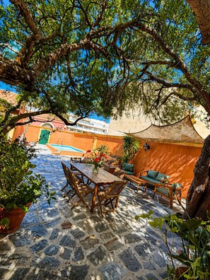 A courtyard with a stone floor, wooden furniture, and a pool in the background. - VILLA ANTONIA Charming house with heated pool - Calvi town center. (Calvi)