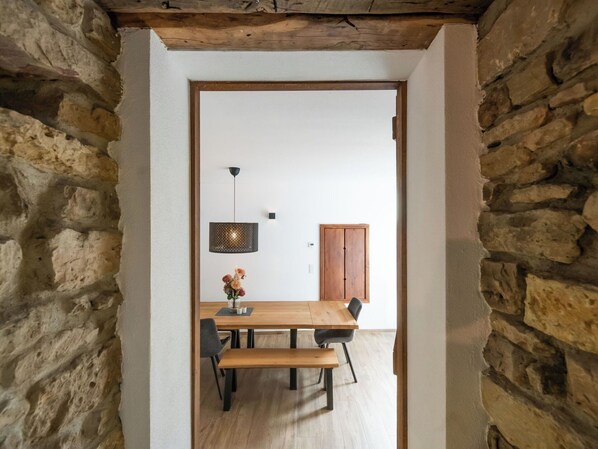 Un vano de puerta en piedra que da a un comedor con una mesa de madera, sillas y una lámpara colgante.