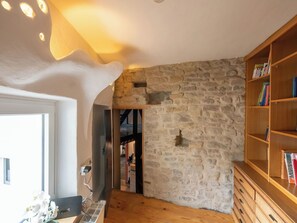 Una habitación con pared de piedra, una estantería de madera y una puerta que da a otra estancia.