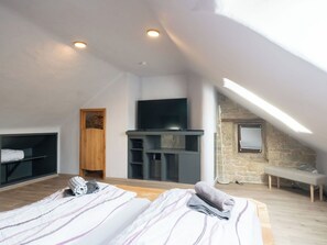Un dormitorio con dos camas, televisión, pared de piedra y puerta de madera.