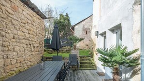 A wooden deck with a table and chairs, a potted plant, and a stone wall. - Wonderful private villa for 10 guests with TV and terrace (Rittersdorf)
