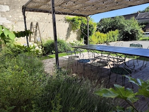 An outdoor patio with a table and chairs, surrounded by greenery and a stone wall.