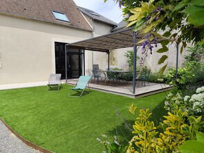 Une terrasse avec des meubles d’extérieur, un espace salon abrité et une pelouse bien entretenue.