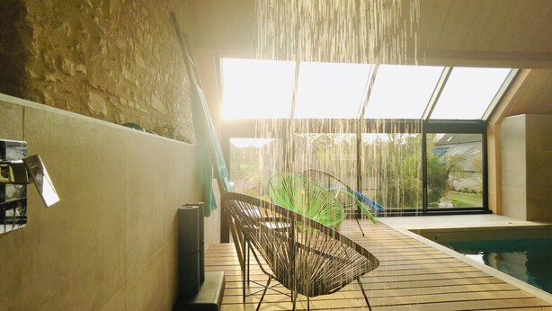 A modern interior with a wooden floor, a green chair, a staircase, and a view of a pool through large windows. - Charming Holiday Home 'Les Griottes Gîte de Charme' with Indoor Pool (Verdigny)