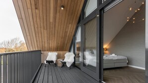 En balkon med to hvide stole, træloft og en seng med udsigt.