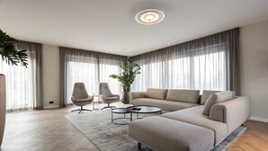 En moderne stue med en hjørnesofa, to lænestole, et sofabord og et stort vindue med gardiner.