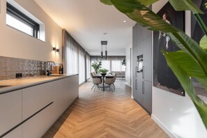 Une cuisine moderne avec un parquet en chevrons, un coin repas avec une table ronde et des chaises, et une grande fenêtre avec des rideaux.