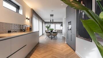 Een moderne keuken met een visgraatvloer, een eetgedeelte met een ronde tafel en stoelen, en een groot raam met gordijnen.