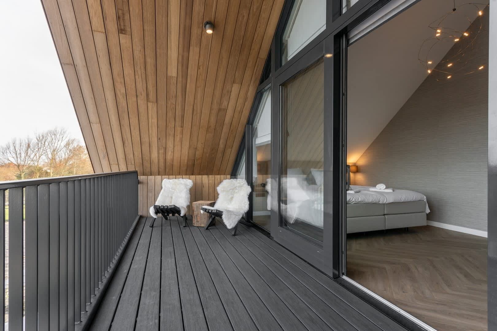 Een balkon met twee witte stoelen, een houten plafond en een bed met uitzicht.