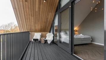 Een balkon met twee witte stoelen, een houten plafond en een bed met uitzicht.