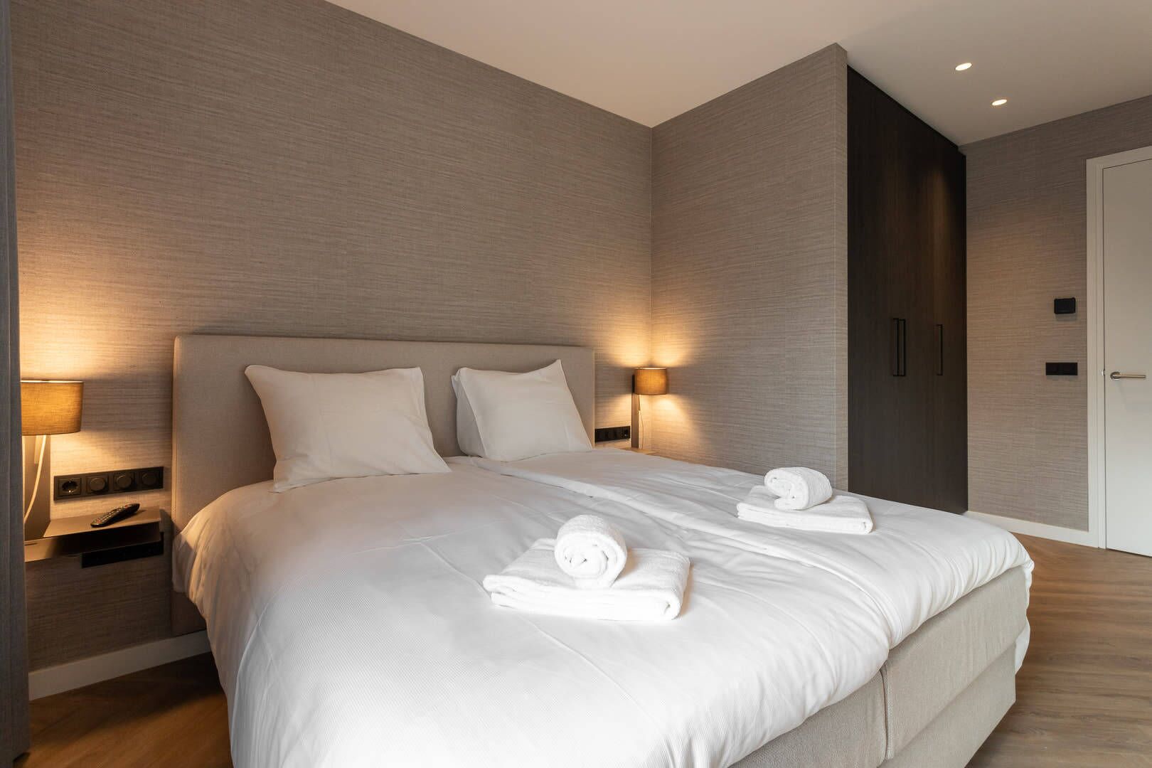 A modern hotel room with a large bed, bedside lamps, and neatly folded towels.