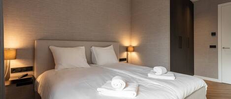 A modern hotel room with a large bed, bedside lamps, and neatly folded towels.