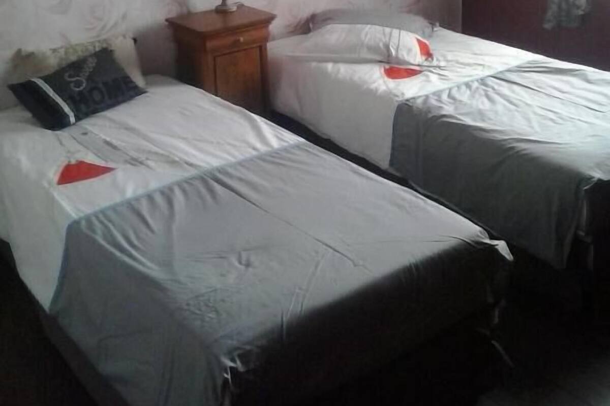 A room with two beds, a nightstand with a lamp, and a window with curtains.