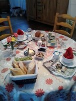 Una mesa redonda para comer con mantel floreado, diferentes alimentos y un periódico.