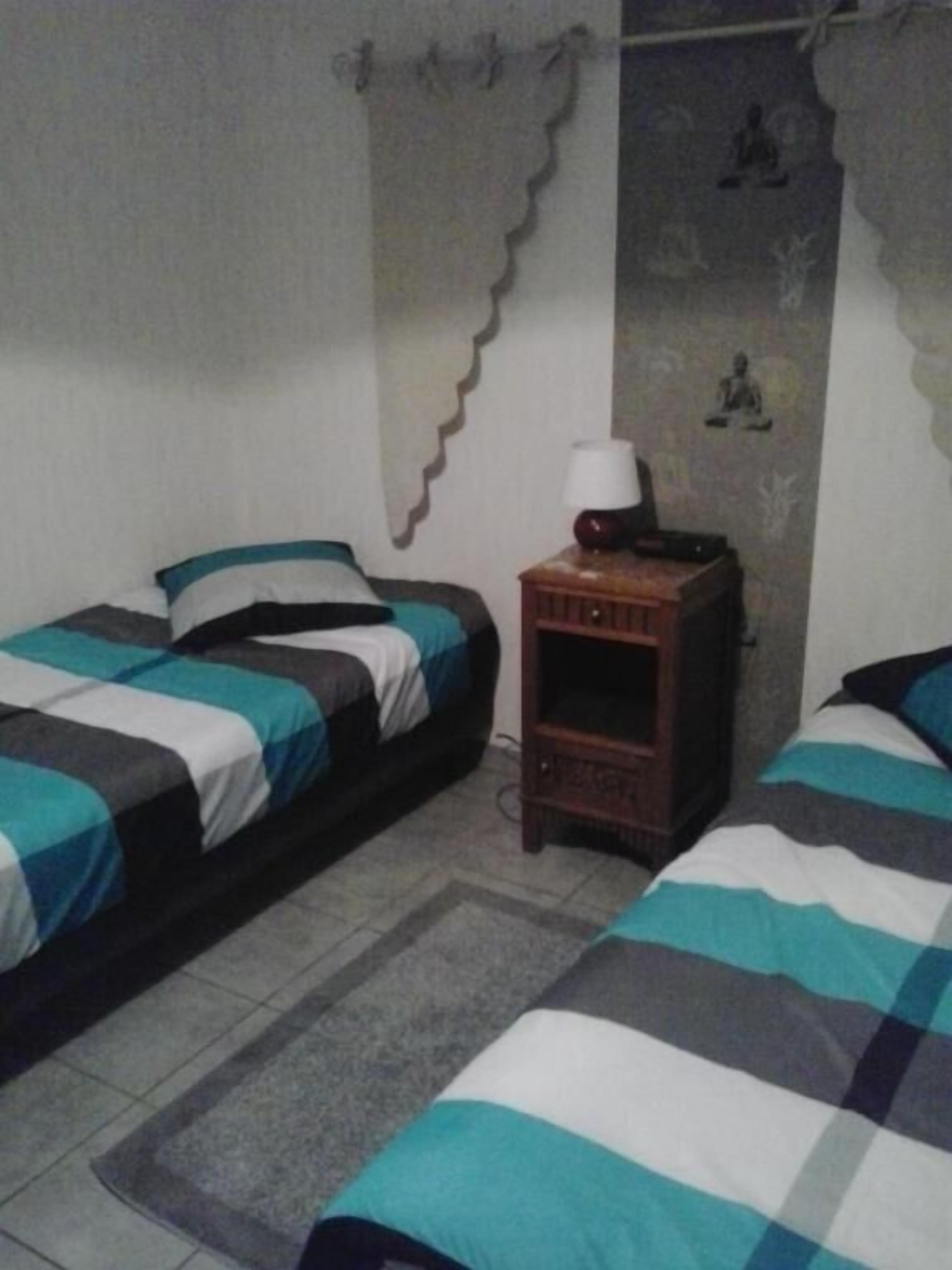Quarto com duas camas, uma mesinha com abajur, e parede com um padrão decorativo.