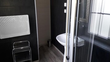 Un baño moderno con cabina de ducha de vidrio, un lavamanos blanco y un taburete de metal.