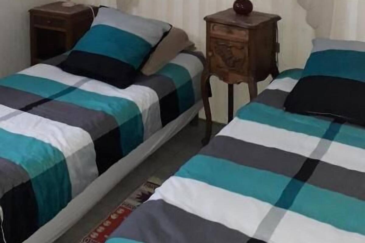 A bedroom with two beds, a nightstand, a lamp, and a wall with a curtain.