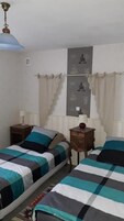 Un dormitorio con dos camas, una mesita de noche, una lámpara y una pared con cortina.