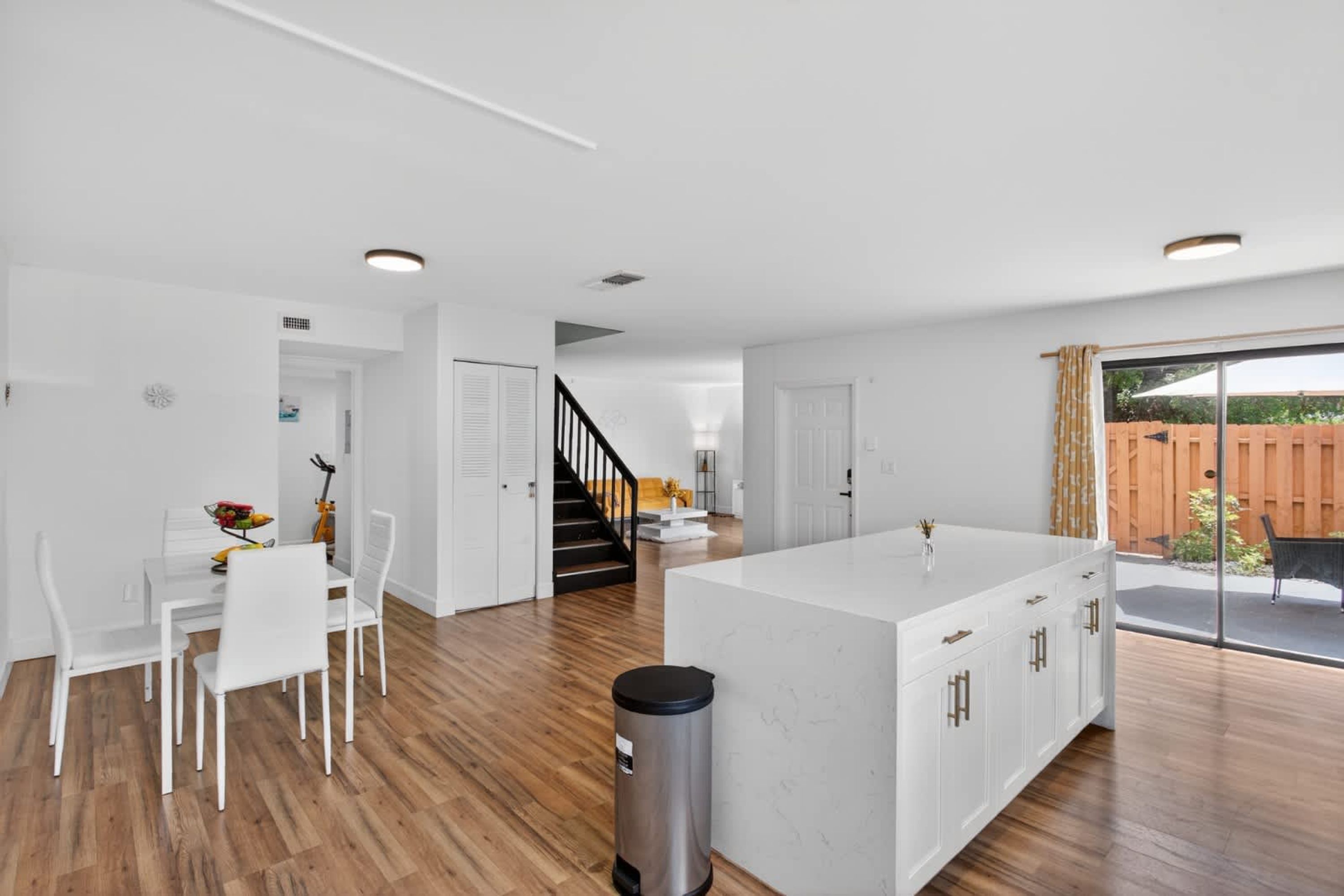 A modern kitchen with white cabinetry, a central island, and a dining area with white chairs.