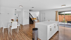 Een moderne keuken met witte kasten, een centraal eiland en een eethoek met witte stoelen.
