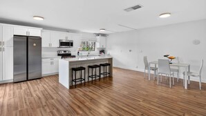 Een moderne keuken met witte kasten, een roestvrijstalen koelkast, een magnetron, en een eethoek met witte stoelen en een kleine tafel.
