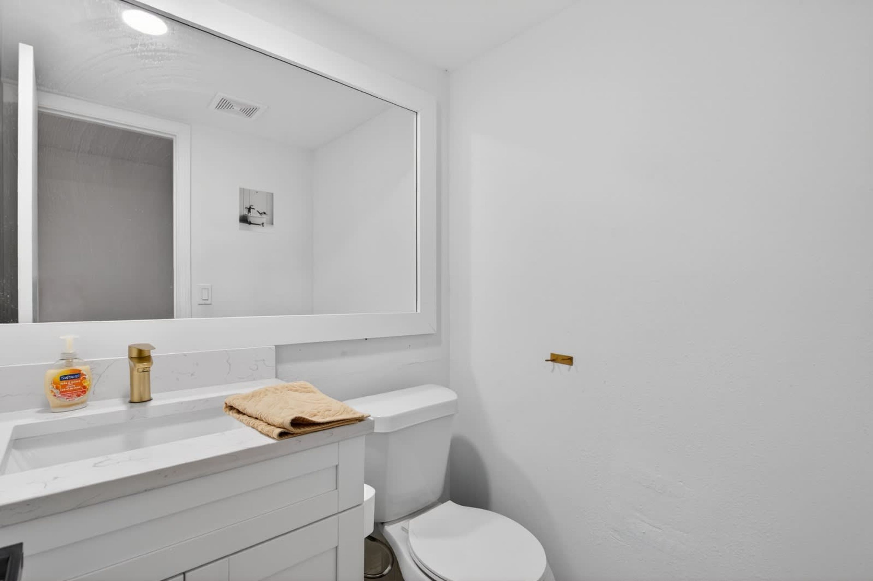 A bathroom with a white sink, a mirror, a toilet, and a towel on the counter.