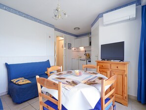 Ein gemütlicher Wohnraum mit Esstisch, Stühlen, einer Couch, einem Fernseher und einer kleinen Küchenzeile im Hintergrund.