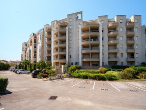 Ein mehrstöckiges Wohnhaus mit Balkonen, einem Parkplatz und Grünflächen.