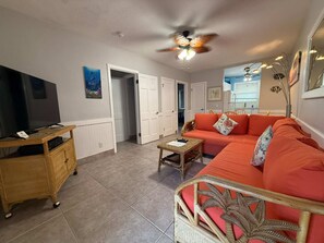 Uma sala de estar com televisão, ventilador de teto, sofá e mesa de centro.