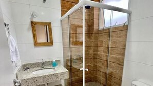 A bathroom with a glass shower enclosure, a sink with a mirror, and a toilet. - Residencial 220 Maresias (São Sebastião)