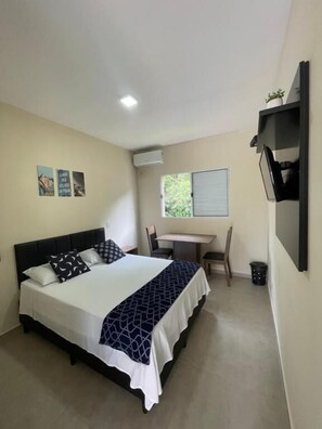 A bedroom with a bed, a desk, and a chair. There is a window with a view of greenery outside. - Residencial 220 Maresias (São Sebastião)