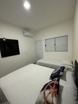 A single bed with a white mattress, a pillow with a nautical design, and a wall-mounted air conditioner. - Residencial 220 Maresias (São Sebastião)
