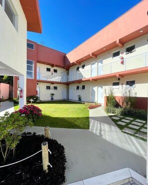 A multi-story building with a courtyard, outdoor seating, and a small garden area. - Residencial 220 Maresias (São Sebastião)