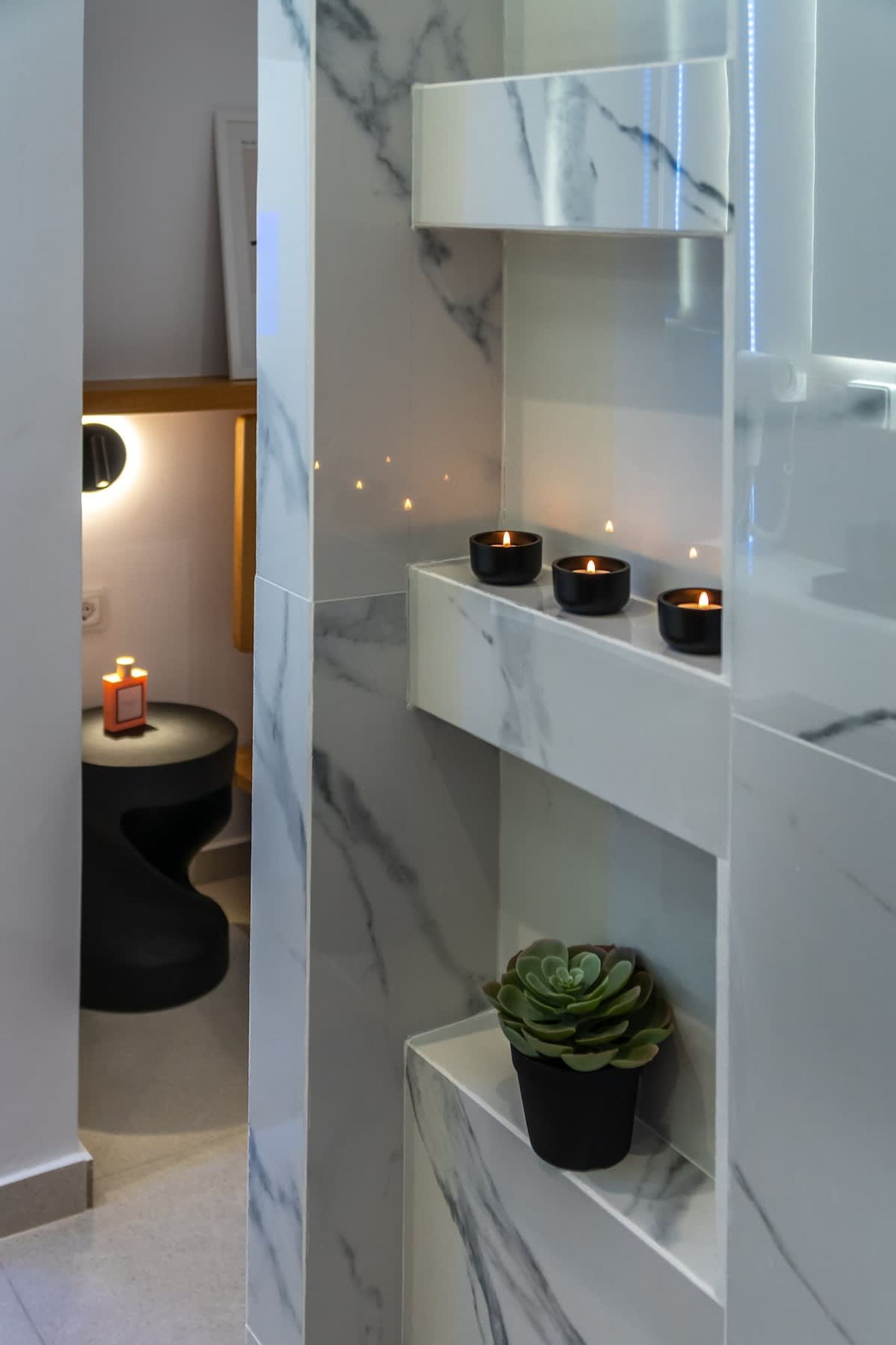 A bathroom with a marble wall, a black sink, and three lit candles on a shelf.