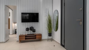 Ein modernes Zimmer mit Flachbildfernseher, einer Holzkonsole, einem Blumentopf und einer Tür.