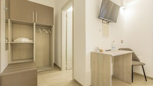 Une chambre d’hôtel dotée d’un dressing, d’un bureau avec une chaise et d’un téléviseur fixé au mur.