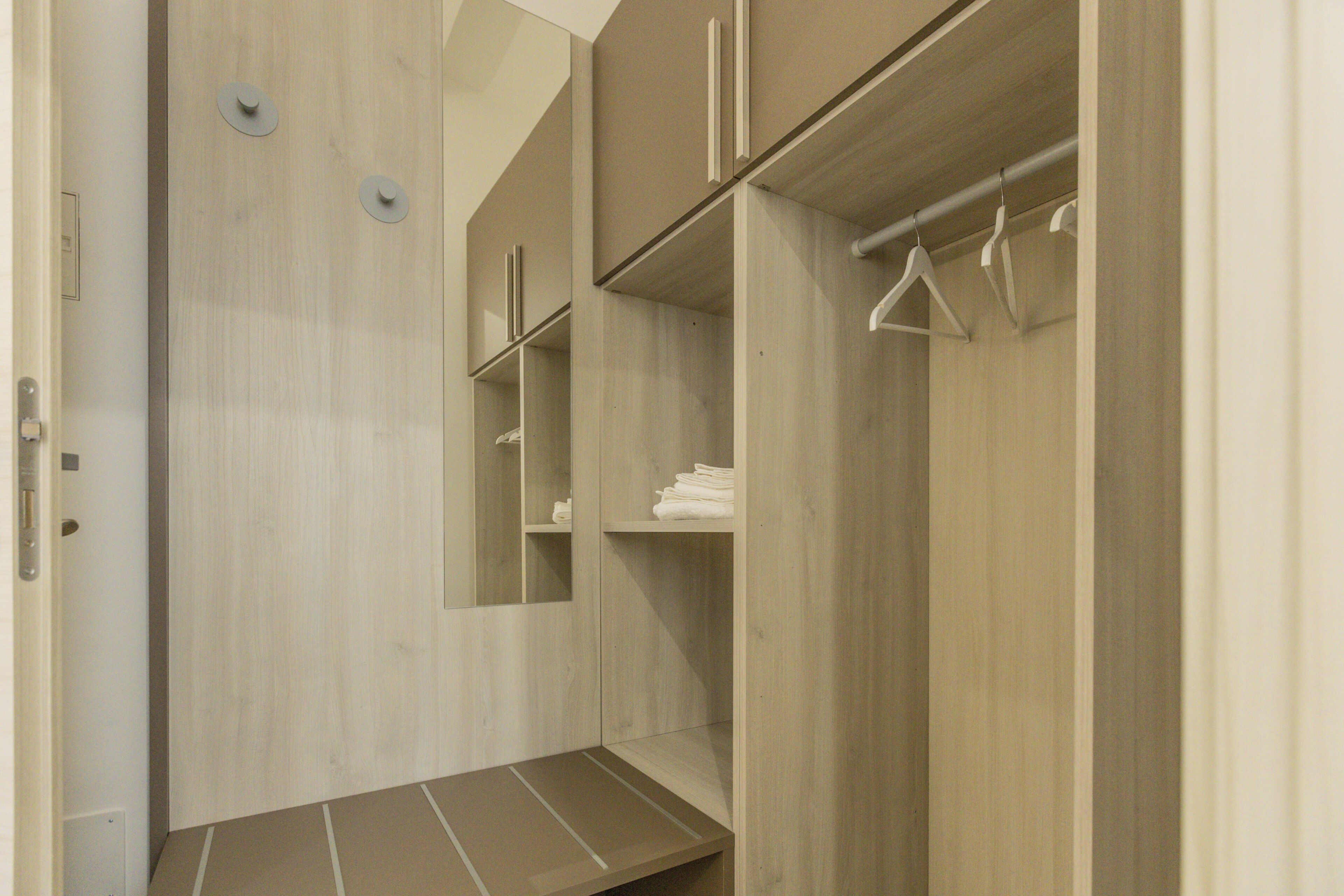 A walk-in closet with wooden doors, a mirror, and hanging clothes.