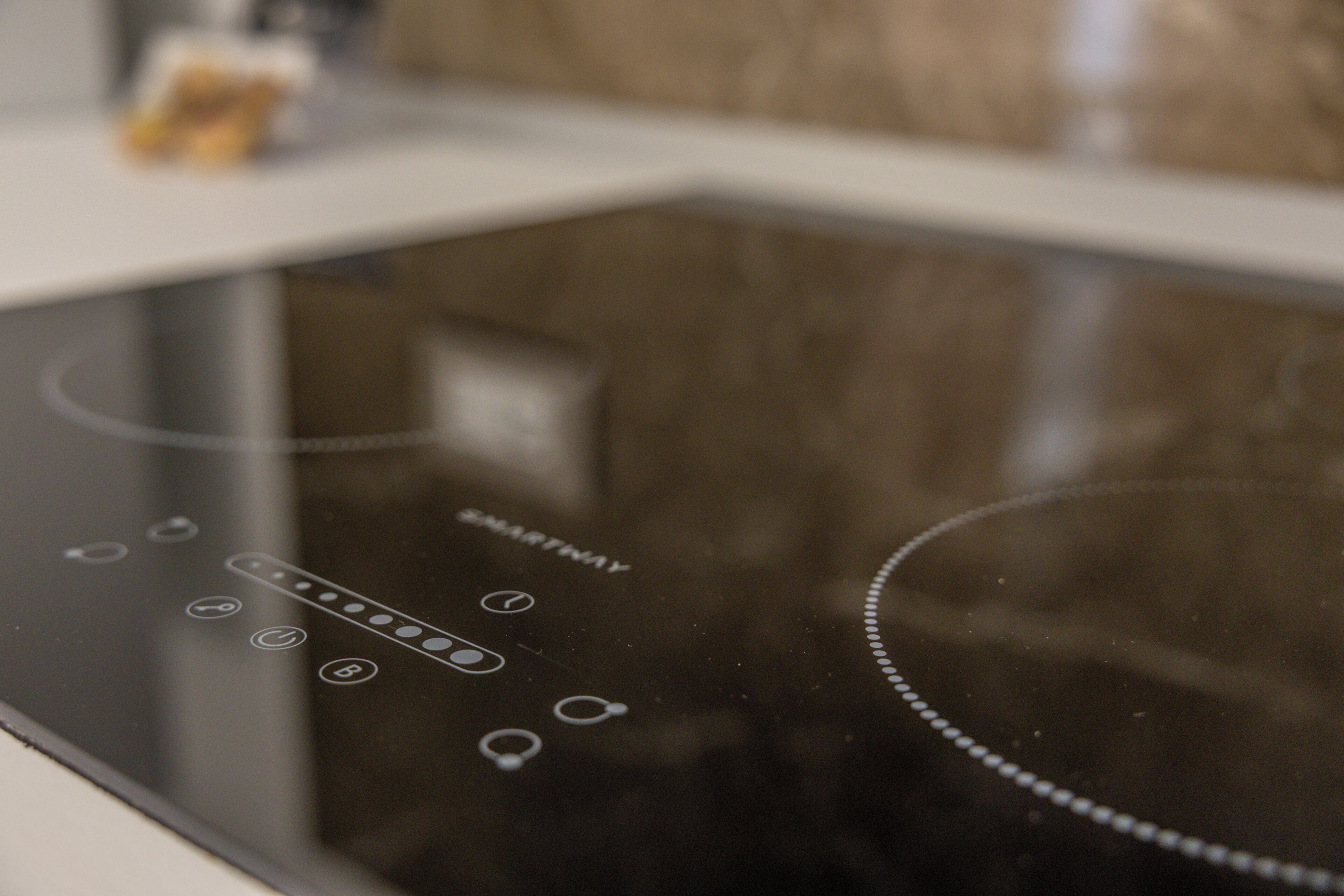 A kitchen with a black induction cooktop and a control panel with various buttons and a display.