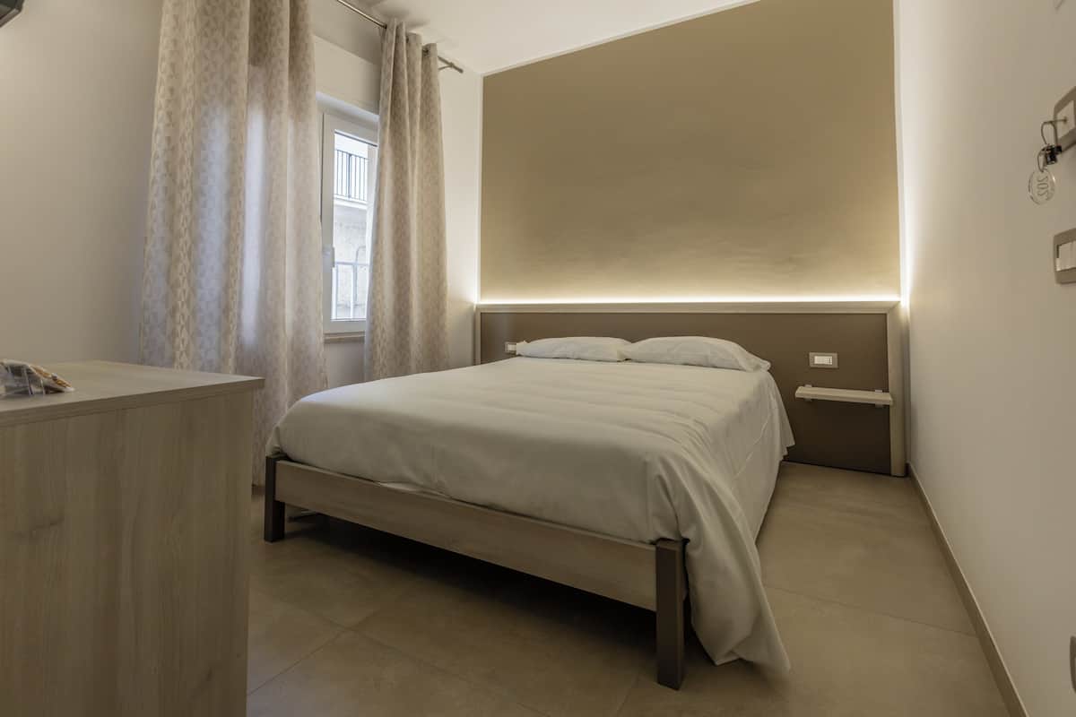 A bedroom with a bed, bedside tables, a desk, and a window with curtains.