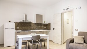 Une cuisine compacte avec un réfrigérateur blanc, un pare-feu en marbre, une cuisinière à gaz et un coin repas comprenant des chaises et une table.