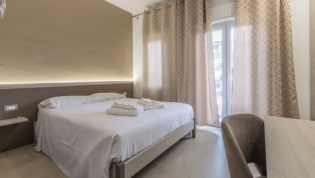 Une chambre d’hôtel avec un lit, une chaise, une table de chevet et une fenêtre avec des rideaux.